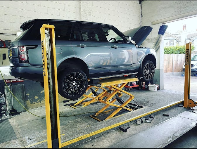 A head on view of a silver Range Rover on a yellow ramp with the bonnet open.