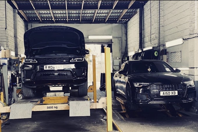 A black Audi and a black Range Rover on ramps side by side. 