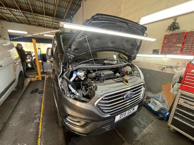 A silver Ford van with the bonnet open, exposing the engine. 