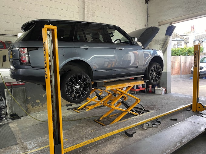 A side view of silver Range Rover on a ramp with the bonnet open.