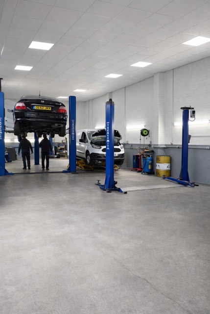 A white car on a ramp with a technician working underneath.